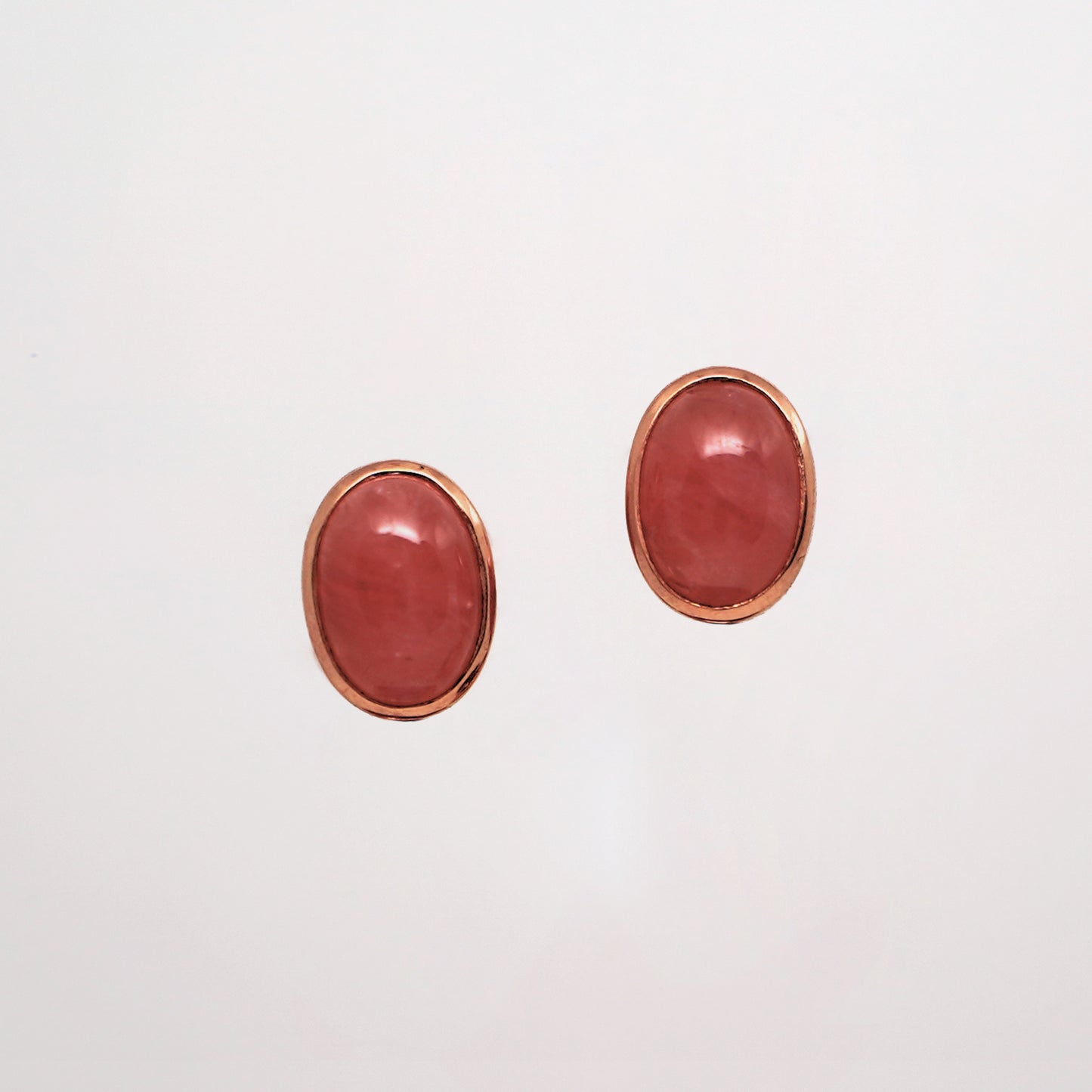 Rhodochrosite Stud Earrings are a pair of pink oval earrings with rose gold frames on a light gray background