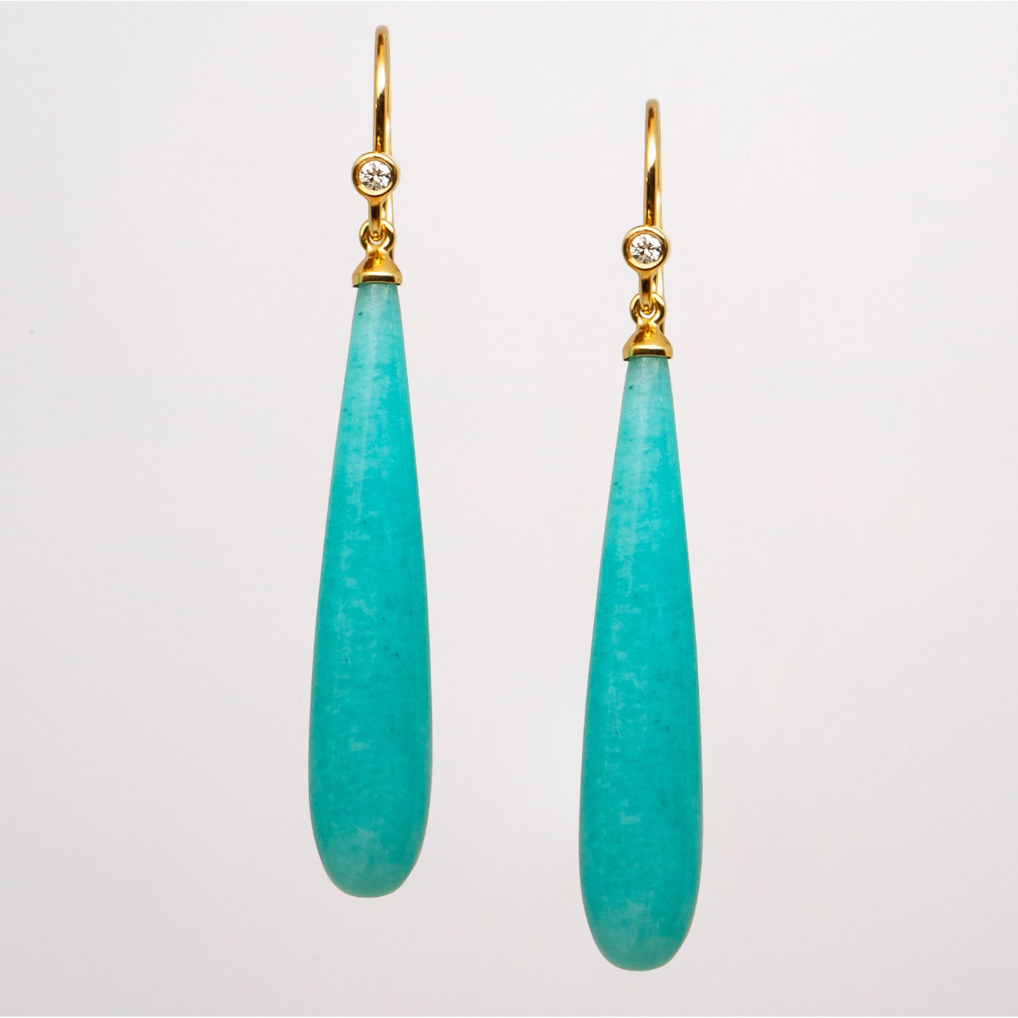 Pair of turquoise teardrop earrings with gold hooks and diamonds on a light gray background