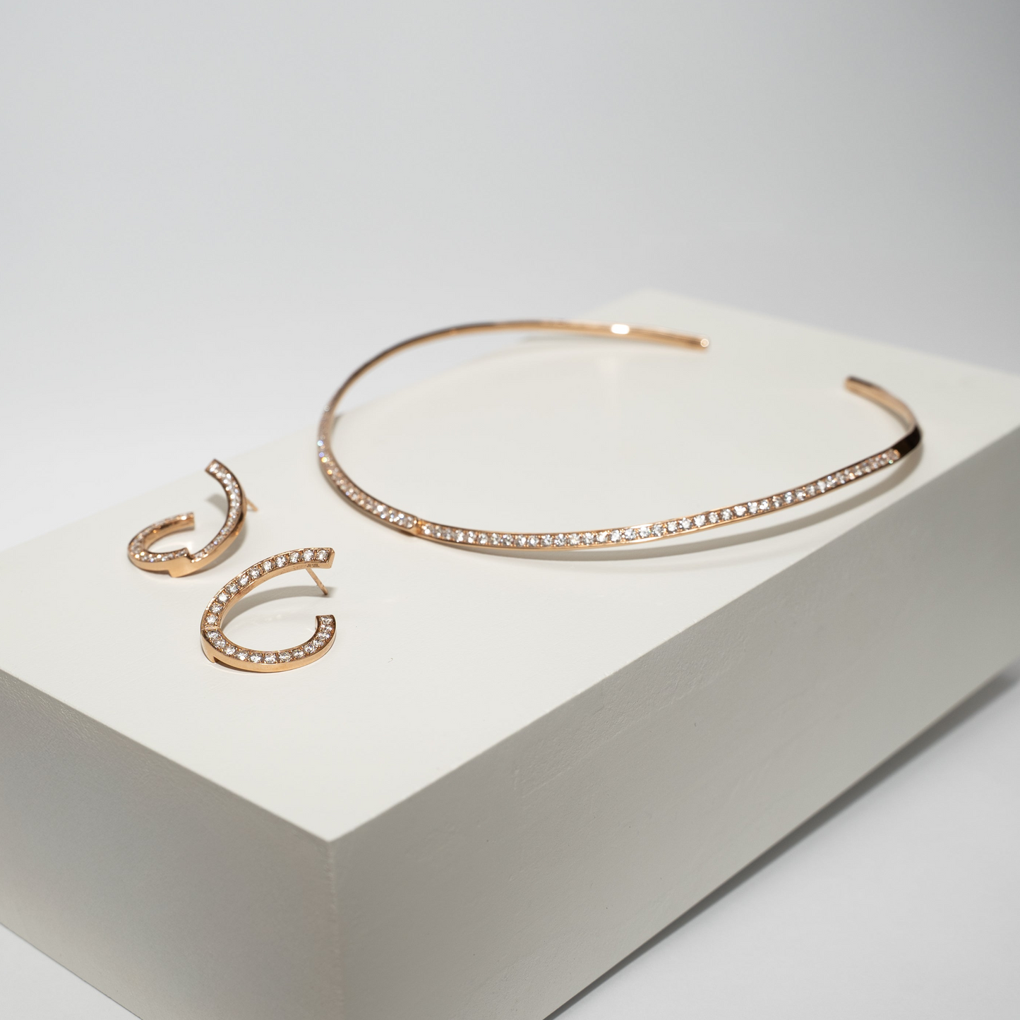 Rose Gold necklace and earrings with diamonds on a white box against a gray background