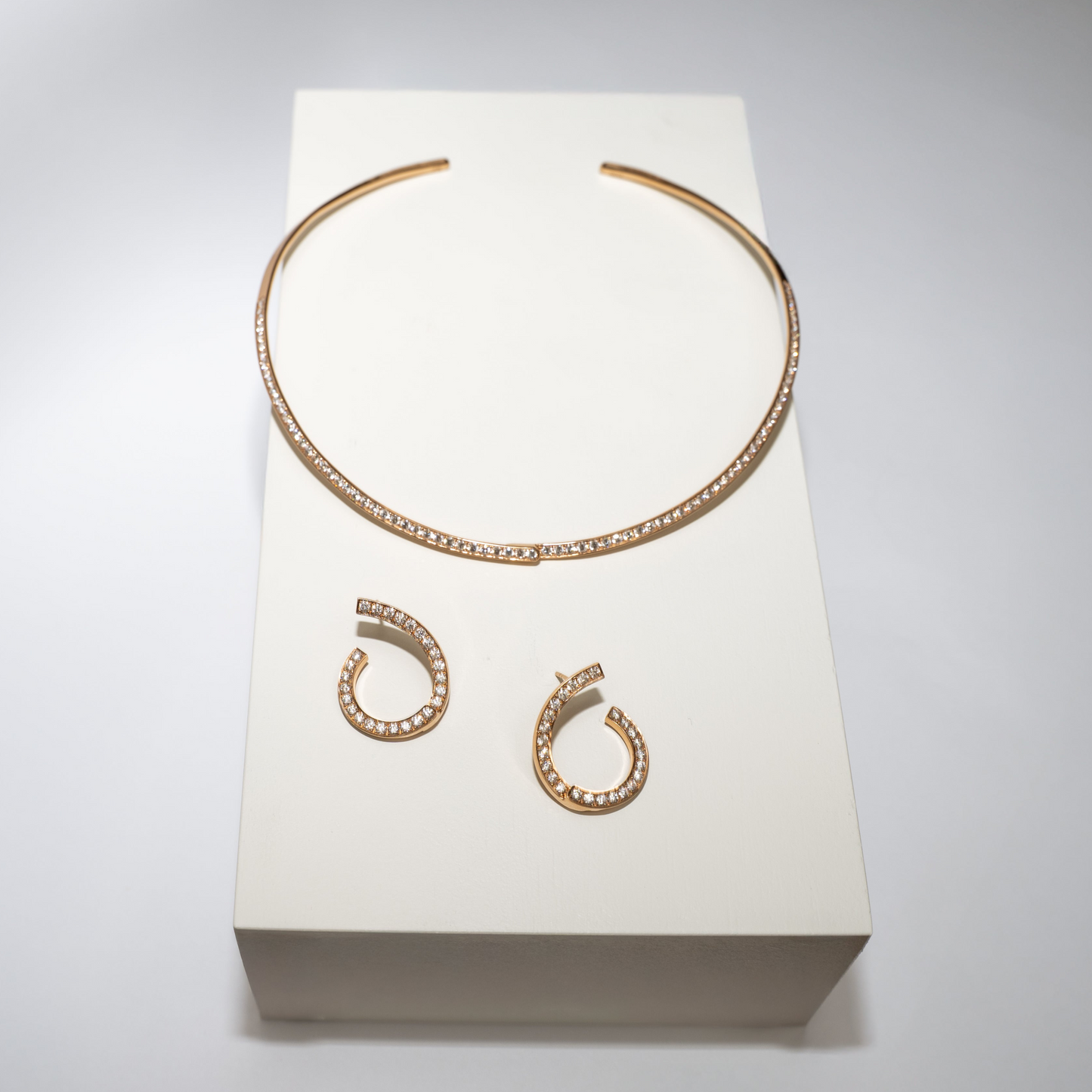 Rose Gold necklace and earrings with diamonds on a white box against a gray background