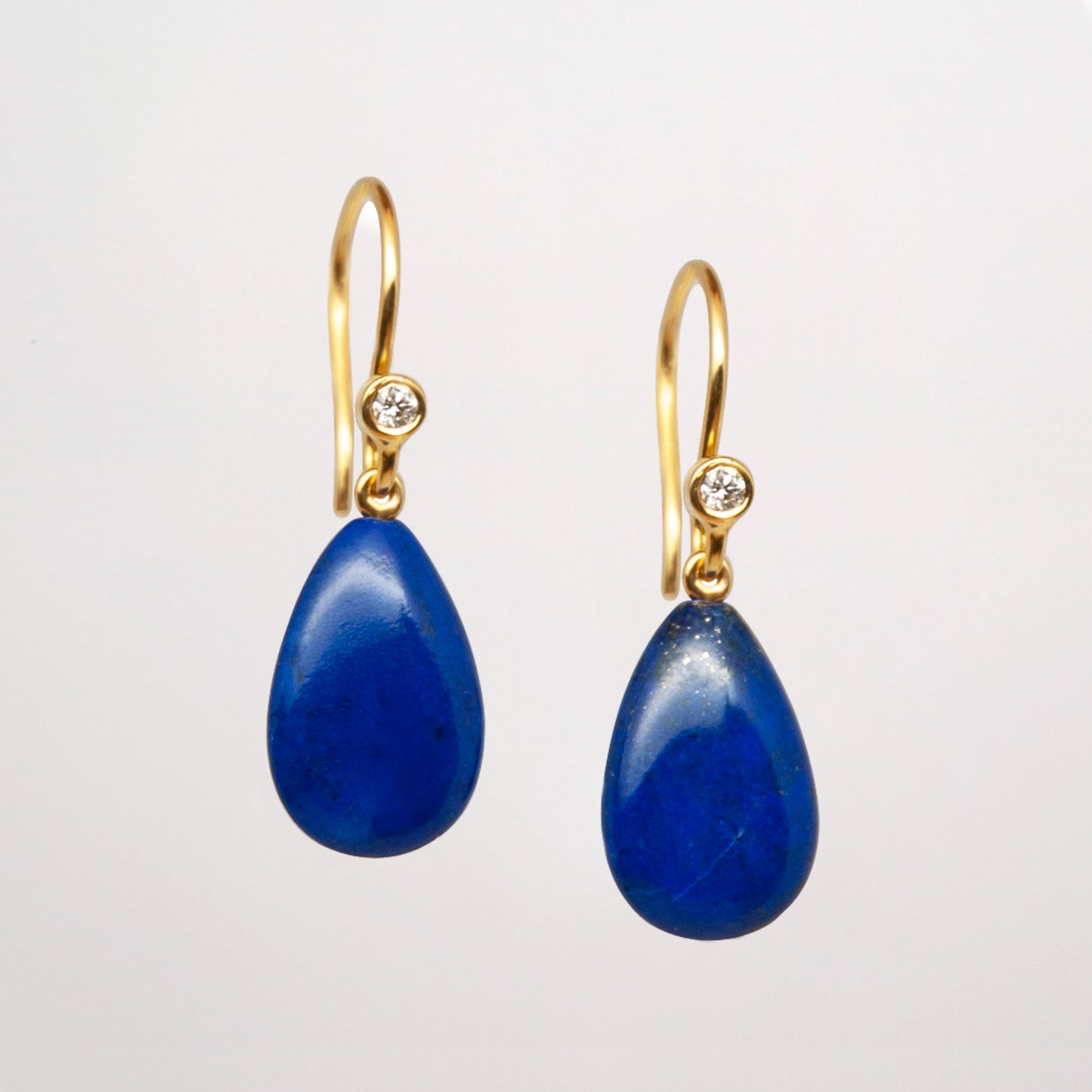 Pair of lapis lazuli gold earrings with blue teardrop stones and diamonds on a grey background