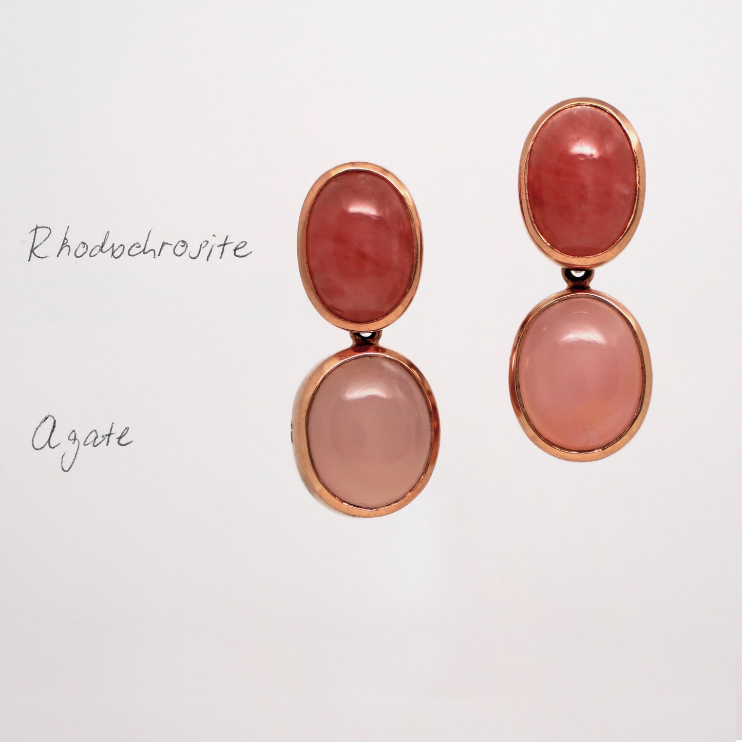 Pair of gemstone earrings with pink stones set in rose gold on a light gray background